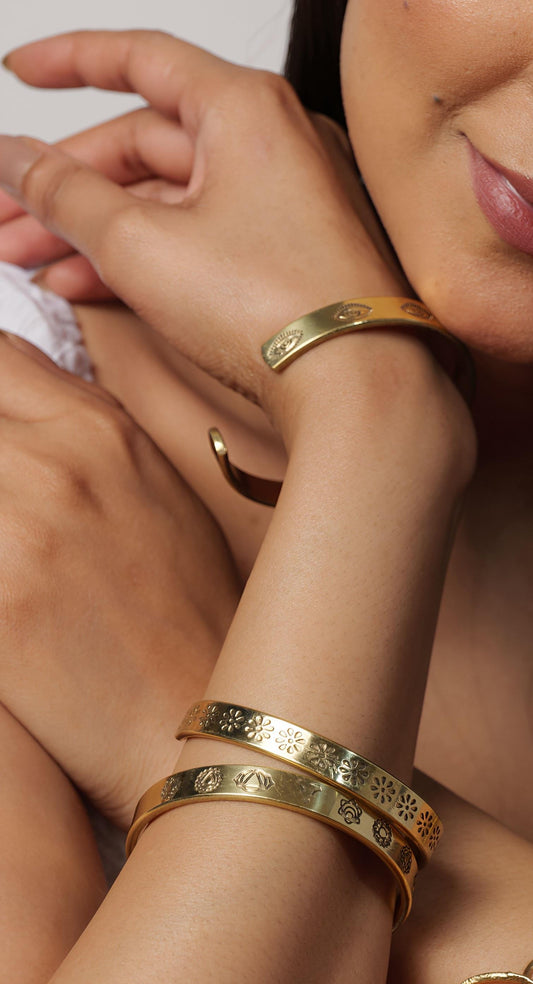 Woman wearing multiple gold bracelets on her wrist with a neutral background